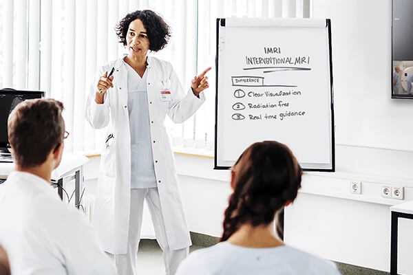 A presenter pointing at a display board describing the benefits of iMRI as she explains to two listeners.