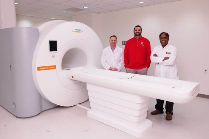 Three men posing next to a Siemens MRI machine.